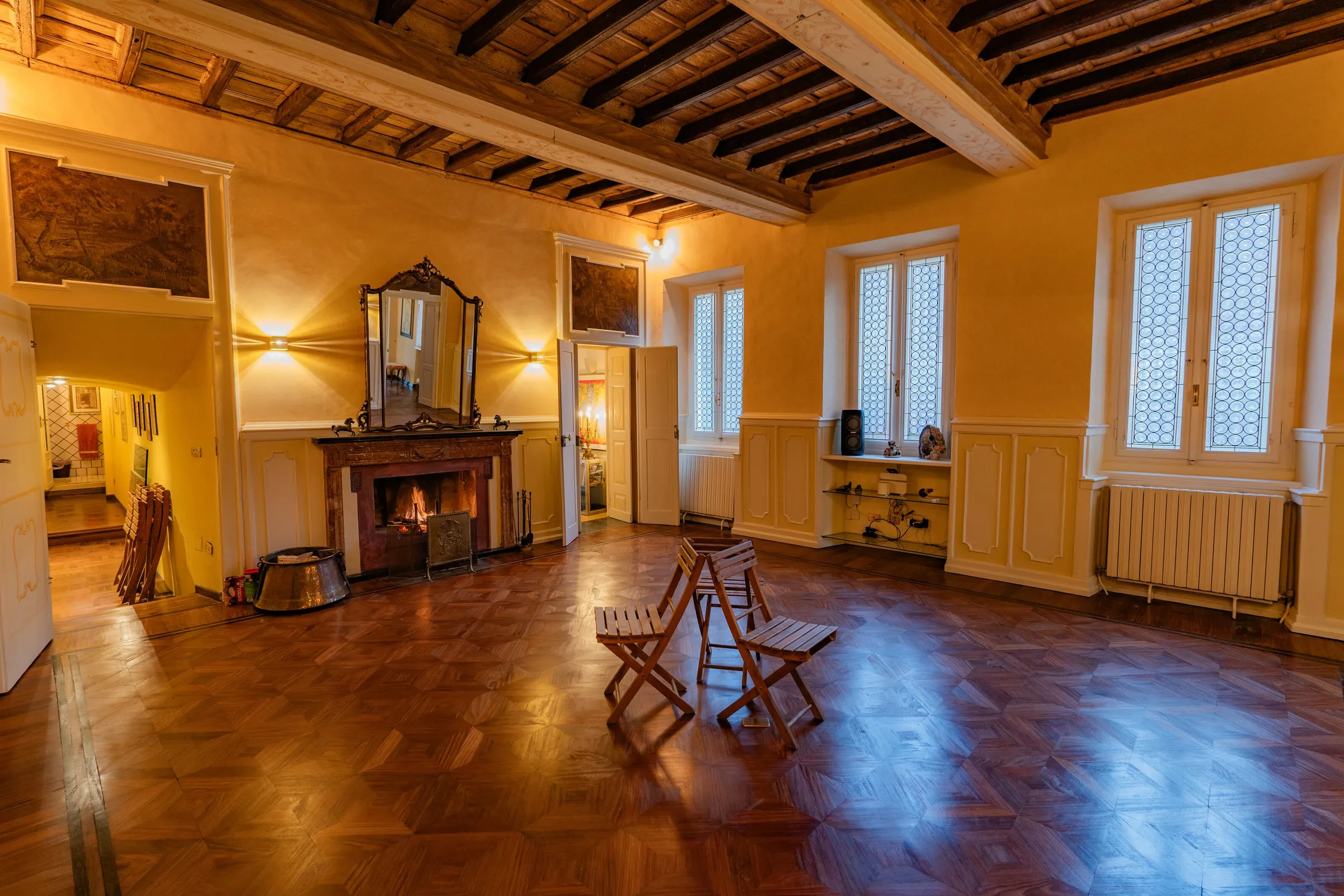 La sala antica con il soffitto a cassettoni, il camino acceso, la specchiera dorata e le sovrapporte dipinte